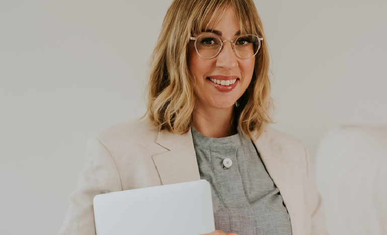 Melissa Bourgeois, a woman with shoulder length blonde hair and wearing glasses, poses holding a tablet.