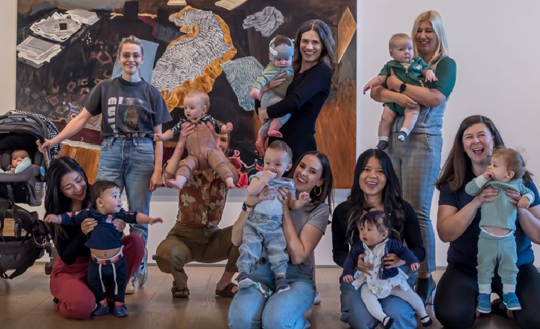 A group of women laywers and their children pose in front of a piece at an art gallery