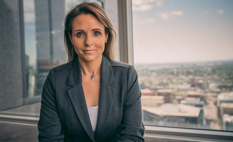 Bianca Kratt, sitting in a grety suit jacket in front of a window