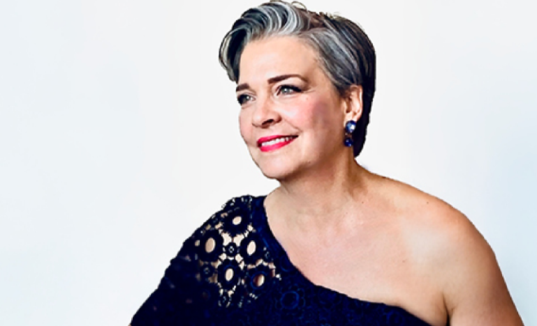 Patricia Hiebert, a woman with short, dark hair, poses wearing a navy blue lace dress.
