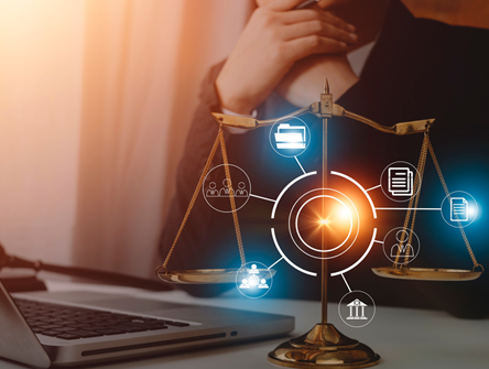 A person sits at a desk with a laptop, behind a brass balance scale and digital legal icons representing law, documents, and communication.