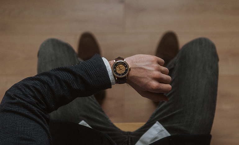 a photo, taken from above, of seated man looking at his watch