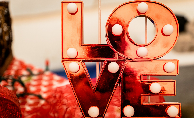 A decorative sign with the word LOVE in red, illuminated by round white lights, against a blurred background.